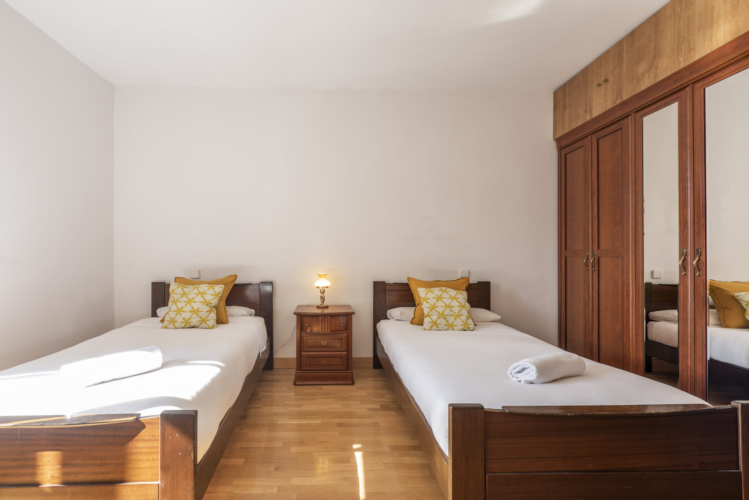 A bedroom with matching wooden single beds with a built-in wardrobe with central mirror doors